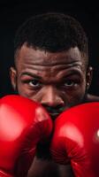 A determined boxer stands in a training pose, holding red boxing gloves close to his face, showcasing intensity and focus before an upcoming match. photo
