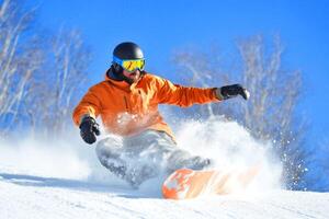 A snowboarder in an orange jacket skillfully carving through fresh snow on a bright winter day in a mountainous landscape photo