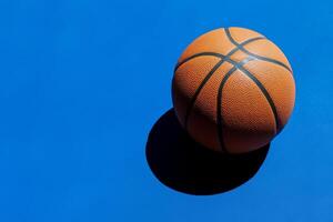 A basketball resting on a vibrant blue court surface, showcasing its texture and shadow during sunny daylight photo