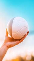 A hand holds a volleyball against a vibrant sky during sunset at a beachside location photo