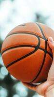 A hand gripping a basketball prepares for a shot in a sunny outdoor court surrounded by green trees photo