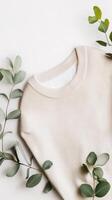 A neutral-toned sweater surrounded by fresh eucalyptus leaves arranged on a light background at a home styling session photo