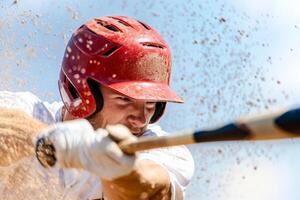 A baseball player swings a bat, kicking up dirt during a game in a sunny stadium on a warm afternoon photo