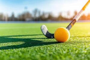 A field hockey stick poised to hit a bright orange ball on a sunny day at a well-maintained sports field photo