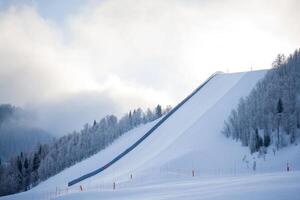 Snow-covered ski slope under cloudy sky with trees in the background during winter morning light photo