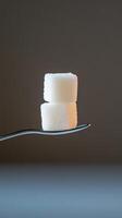 Two white sugar cubes balanced on a spoon against a dark background photo