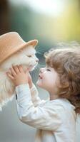 A child joyfully interacts with a fluffy white cat while wearing a straw hat outdoors on a sunny day in a serene setting photo