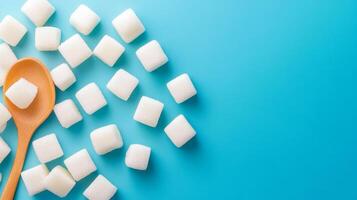 White sugar cubes scattered on a bright blue background with a wooden spoon resting among them photo