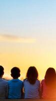 Children watching a beautiful sunset together while sitting on a ledge during a warm summer evening photo