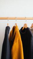 A collection of cozy sweaters hanging on a wooden rack in a stylish indoor setting during the day photo