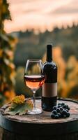 Elegant glass of rose ine beside a bottle and fresh grapes on a wooden barrel in a vineyard at sunset photo