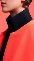 A close-up of a modern fashion jacket with a vibrant coral outer layer and a contrasting black high collar on a neutral backdrop photo