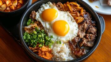 A sizzling hot stone bowl filled with delicious rice, grilled beef, fresh vegetables, and sunny-side-up eggs at a local restaurant photo