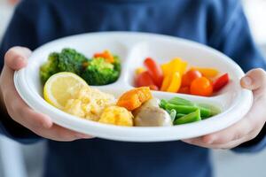 A child enjoys a balanced meal with broccoli, colorful peppers, and a lemon wedge on a white divided plate photo