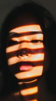 A close-up of a woman's face illuminated by shadows created by sunlight filtering through window blinds in a warm setting photo