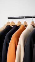 A collection of stylish hoodies hanging on a rack showcasing various colors in a minimalistic setting photo