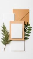 An elegant arrangement of blank stationery, an envelope, and green foliage placed on a light background for creative inspiration photo