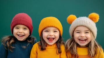 Three young girls wearing colorful knit hats share bright smiles against a teal background during a joyful winter day photo