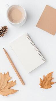 A cozy autumn workspace with a cup of coffee, notepad, and fallen leaves on a white table photo