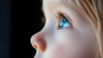 A child's close-up gaze reveals bright blue eyes and delicate features against a dark background during a quiet moment of reflection photo