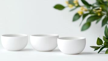 Three elegant white bowls arranged on a light surface next to fresh greenery and delicate flowers in a serene setting photo