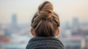 A woman with a bun hairstyle looks out over a city skyline during the early morning hours with a soft haze hanging in the air photo