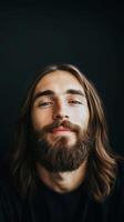 A young man with long hair and a beard smiles confidently against a dark background, showcasing a relaxed and charming demeanor photo