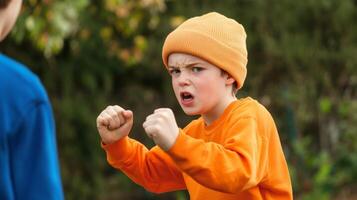 Young boy in an orange shirt and hat showing anger while facing another child outdoors in a backyard during daylight photo