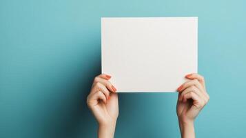 Person holding a blank white sheet of paper against a blue background, showcasing design projects or presentations photo