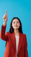 Young woman in a red blazer with long hair pointing up against a vibrant blue background in a bright and cheerful setting photo