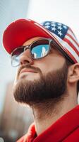 A man wearing sunglasses and a cap with the American flag gazes upward in an urban setting during the daytime photo