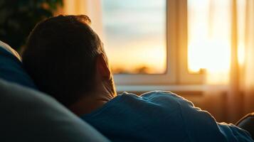 Man relaxing on a couch by the window watching the sunset in a cozy living room during evening hours photo