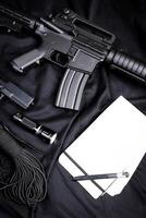 Rifle, gun, knife with sheath, compass and notebook with pen on on black cloth photo