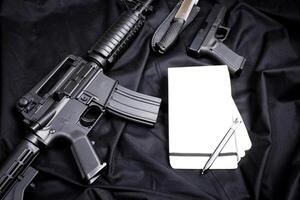 Rifle, gun, knife with sheath, compass and notebook with pen on on black cloth photo