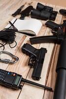 Assault rifle, gun, knife with sheath, compass and notebook with pen on table. photo