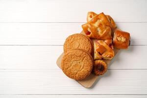 Assortment of baked goods on a wooden tray with a rustic white background, featuring cookies and pastries photo