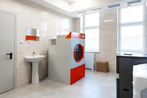 Modern laundry area featuring a red and gray washing machine in a bright, clean environment with natural light filtering through windows photo