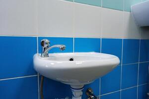 Small white sink with chrome faucet in a tiled bathroom setting during daylight hours photo