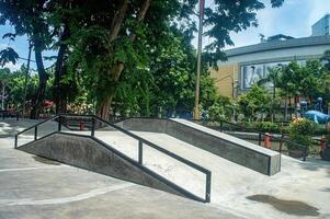 A modern skate park with ramps and rails, surrounded by lush trees and an urban backdrop, perfect for skateboarding and BMX enthusiasts, Indonesia, 12 January 2025 photo