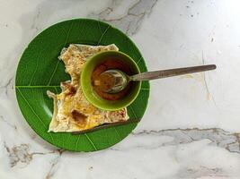 The close up of a traditional Malaysian roti canai served on a green leaf patterned plate with a small bowl of curry sauce and a spoon. The vibrant colors and textures make it visually appealing photo