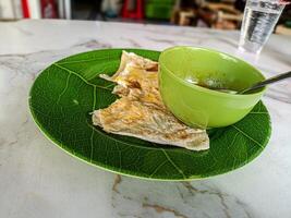 Malaysian roti canai served on a green leaf patterned plate with a bowl of curry. A popular and delicious street food photo