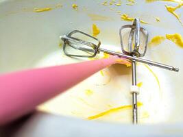 A close up of a mixing bowl with yellow batter remnants and two metal beaters, one with a pink handle, used for baking. This image captures the aftermath of baking photo
