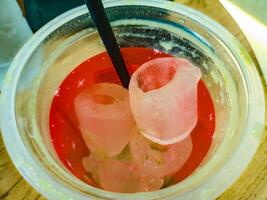 A close up of a red beverage in a plastic cup with large, hollow ice cubes and a black straw. The ice cubes have a unique, cylindrical shape, making the drink visually appealing photo