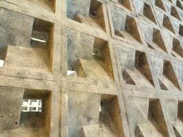 A close up view of a concrete wall with a grid of square recesses, showcasing the texture and geometric pattern of the material. The image highlights the architectural detail and industrial photo