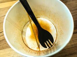An empty bowl with remnants of food and a black spork inside, placed on a wooden surface. The bowl shows traces of seasoning, indicating a finished meal photo