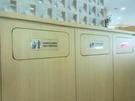 Wooden trash bins with signs in Indonesian urging proper waste disposal, located in a modern, well lit public space. The bins are neatly arranged, emphasizing environmental awareness and hygiene photo