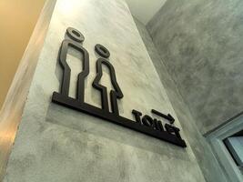 Modern restroom sign on a concrete wall, featuring minimalist male and female figures with the word TOILET and an arrow pointing to the right. Ideal for public facilities photo