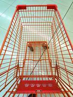 Empty orange shopping cart with grid design, viewed from above, on a tiled floor. Safety instructions visible on the child seat photo