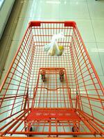 An empty orange shopping cart with a single plastic bag containing fruits, placed in a clean, tiled supermarket aisle photo