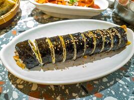 A plate of sliced kimbap, a Korean dish made of rice, vegetables, and meat wrapped in seaweed, garnished with sesame seeds, served on a white plate photo